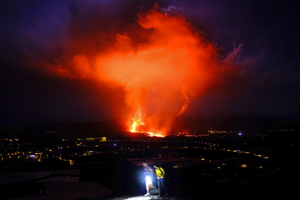 Two people walk as lava spews from a volcano on the Canary island of La Palma, Spain in the early hours of Saturday Sept. 25, 2021. A volcano in Spain's Canary Islands is keeping nerves on edge several days since it erupted, producing loud explosions, a huge ash cloud and cracking open a new fissure that spewed out more fiery molten rock. The prompt evacuations are credited with helping avoid casualties but scientists say the lava flows could last for weeks or months. (AP Photo/Daniel Roca)