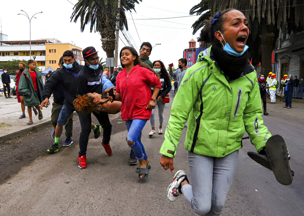 Migrants help a woman who fainted during their eviction by police from Brasil Square where they were living in tents in Iquique, Chile, Friday, Sept. 24, 2021. Hundreds of migrants from Venezuela and Colombia have been living  in the historic sector of the city for over a year. (AP Photo/Ignacio Muñoz)