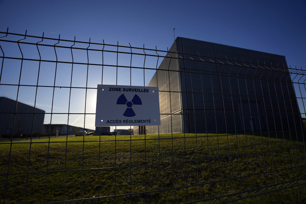 A radioactive sign is placed on the fence of a concrete-sealed warehouse for radioactive waste storage in the Aube region of eastern France, in Soulaines-Dhuys, Friday, Oct. 29, 2021. The site holds low- to mid-level radioactive waste from French nuclear plants as well as research and medical facilities, and its concrete-sealed warehouses are designed to store the waste for at least 300 years. (AP Photo/Francois Mori)
