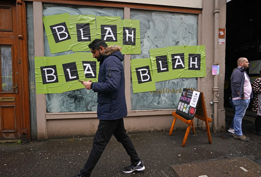 A man walks past a shop with the phrase used by climate activist Greta Thunberg on it's windows as a protest organized by the Cop26 Coalition passes by in Glasgow, Scotland, Saturday, Nov. 6, 2021 which is the host city of the COP26 U.N. Climate Summit. The protest was taking place as leaders and activists from around the world were gathering in Scotland's biggest city for the U.N. climate summit, to lay out their vision for addressing the common challenge of global warming. (AP Photo/Alberto Pezzali)