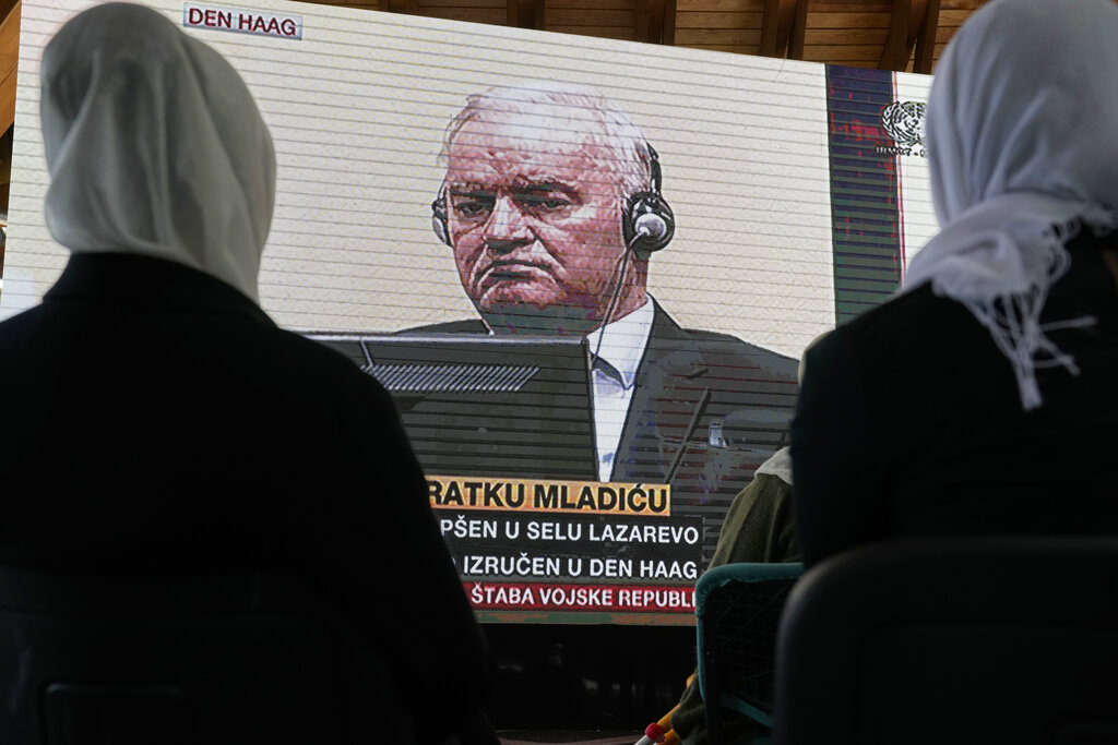 Women from Srebrenica watch a live broadcast from the Yugoslav War Crimes Tribunal in The Hague to learn the verdict for Bosnian Serb military chief Ratko Mladic, on the screen, at the memorial cemetery in Potocari near Srebrenica, eastern Bosnia, Tuesday, June 8, 2021. The United Nations court delivers its verdict in the appeal by former Bosnian Serb military chief Ratko Mladic against his convictions for genocide and other crimes and his life sentence for masterminding atrocities throughout the Bosnian war.(AP Photo/Darko Bandic)