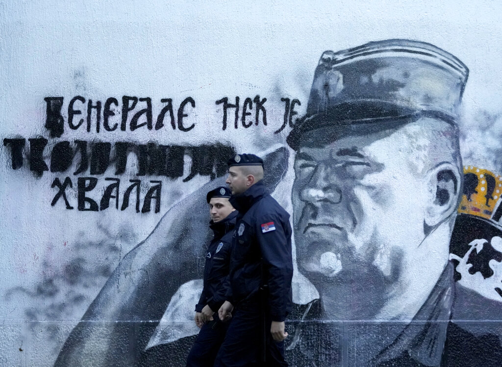Police officers walk by a mural of former Bosnian Serb military chief Ratko Mladic in Belgrade, Serbia, Tuesday, Nov. 9, 2021. Policemen were deployed Tuesday at the site of a large wall painting in Belgrade of convicted Bosnian Serb wartime commander Ratko Mladic which rights activists wanted to remove. The gathering, which was to coincide with the international day of anti-Fascism and anti-Semitism, was banned by the police which said that they were preventing possible clashes between the activists and the right-wing nationalists who consider the Serb general a hero. (AP Photo/Darko Vojinovic)