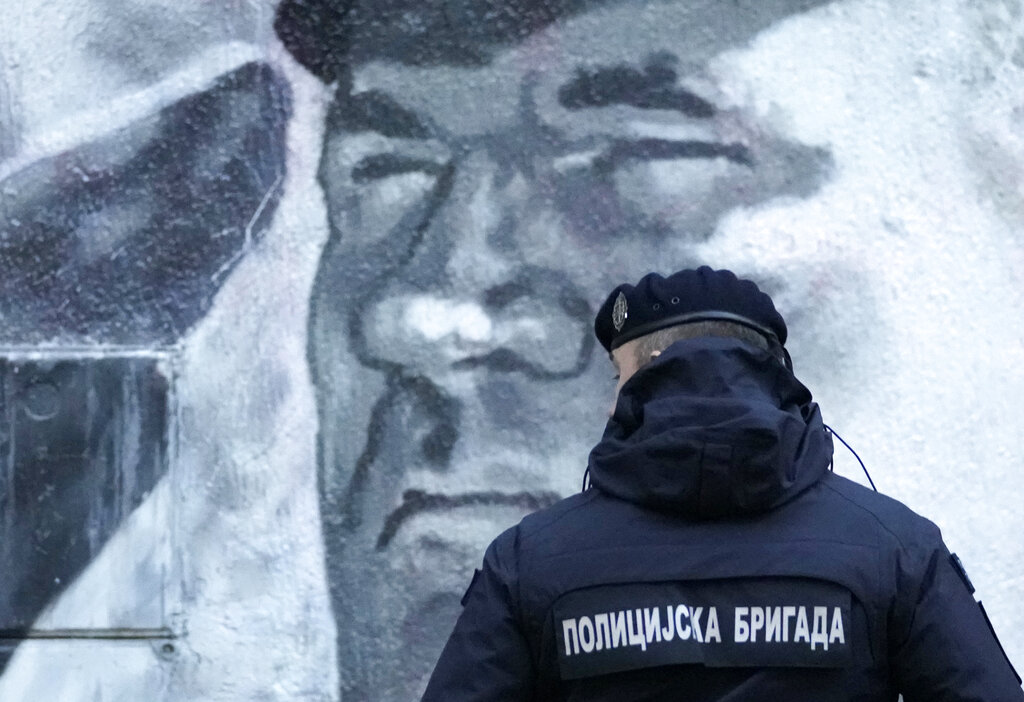 A police officer stands by a mural of former Bosnian Serb military chief Ratko Mladic in Belgrade, Serbia, Tuesday, Nov. 9, 2021. Policemen were deployed Tuesday at the site of a large wall painting in Belgrade of convicted Bosnian Serb wartime commander Ratko Mladic which rights activists wanted to remove. The gathering, which was to coincide with the international day of anti-Fascism and anti-Semitism, was banned by the police which said that they were preventing possible clashes between the activists and the right-wing nationalists who consider the Serb general a hero. (AP Photo/Darko Vojinovic)