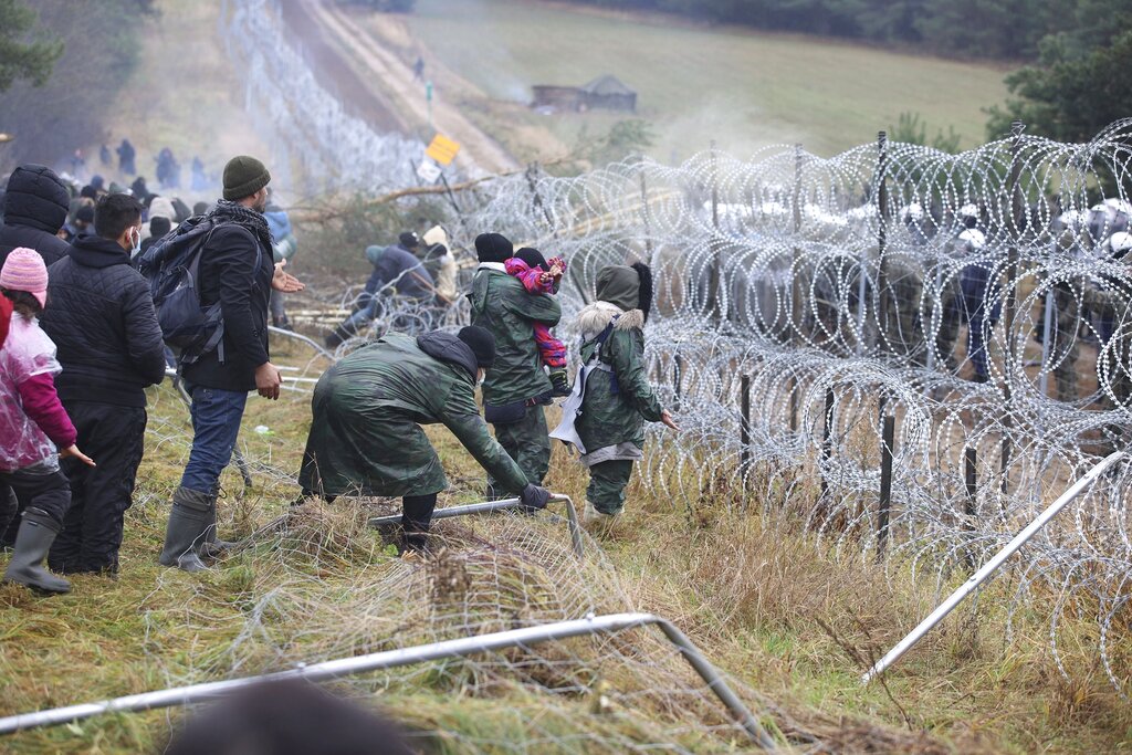 Migrants from the Middle East and elsewhere break down the fence as they gather at the Belarus-Poland border near Grodno, Belarus, Monday, Nov. 8, 2021. Poland increased security at its border with Belarus, on the European Union's eastern border, after a large group of migrants in Belarus appeared to be congregating at a crossing point, officials said Monday. The development appeared to signal an escalation of a crisis that has being going on for months in which the autocratic regime of Belarus has encouraged migrants from the Middle East and elsewhere to illegally enter the European Union, at first through Lithuania and Latvia and now primarily through Poland. (Leonid Shcheglov/BelTA via AP)