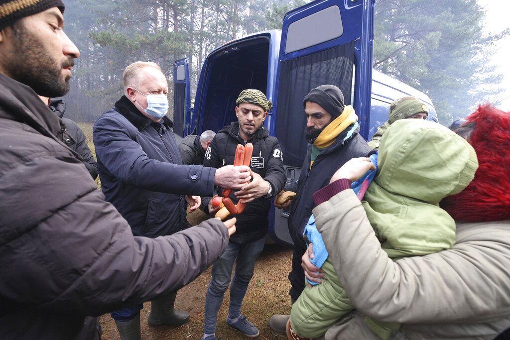 A Belarusian activist, second left, hands over humanitarian aid to migrants from the Middle East and elsewhere gathering at the Belarus-Poland border near Grodno, Belarus, Wednesday, Nov. 10, 2021. The German government says Chancellor Angela Merkel has asked Russian President Vladimir Putin to intervene with Belarus over the migrant situation on that country's border with Poland. Merkel spoke with Putin by phone on Wednesday. (Leonid Shcheglov/BelTA via AP)