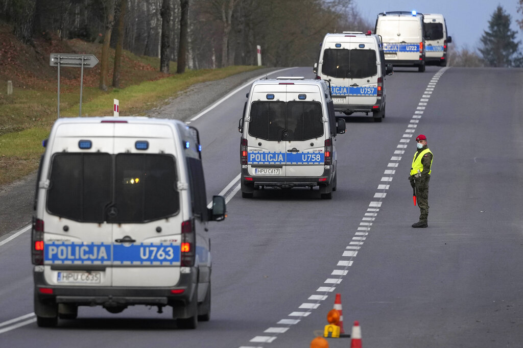 A Polish police officer watches a passing convoy at a checkpoint near the border to Belarus, that was closed because of a large group of migrants camping in the area on the Belarus side who had tried to illegally push their way into Poland and into the European Union, near Kuznica, Poland, Saturday, Nov. 13, 2021. (AP Photo/Matthias Schrader)