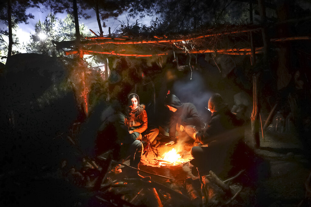 Migrants warm themselves by a fire as they gather at the Belarus-Poland border near Grodno, Belarus, Saturday, Nov. 13, 2021. A large number of migrants are in a makeshift camp on the Belarusian side of the border in frigid conditions. Belarusian state news agency Belta reported that Lukashenko on Saturday ordered the military to set up tents at the border where food and other humanitarian aid can be gathered and distributed to the migrants. (Leonid Shcheglov/BelTA pool photo via AP)