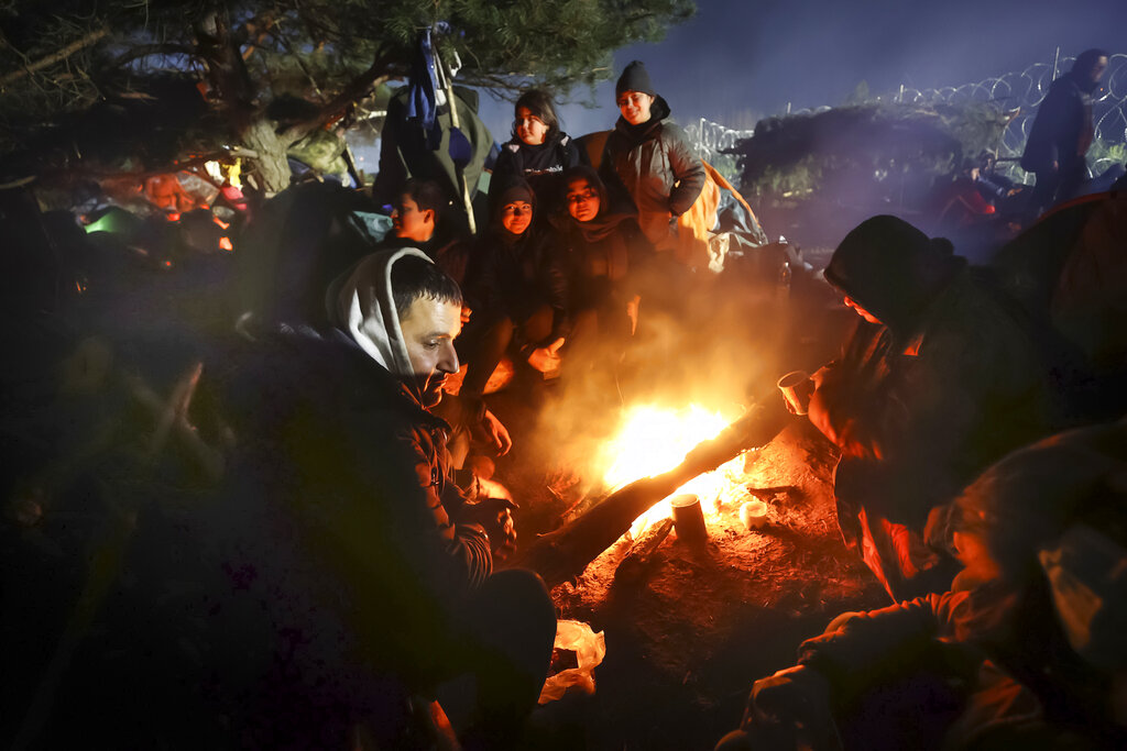Migrants warm themselves by a fire as they gather at the Belarus-Poland border near Grodno, Belarus, Saturday, Nov. 13, 2021. A large number of migrants are in a makeshift camp on the Belarusian side of the border in frigid conditions. Belarusian state news agency Belta reported that Lukashenko on Saturday ordered the military to set up tents at the border where food and other humanitarian aid can be gathered and distributed to the migrants. (Leonid Shcheglov/BelTA pool photo via AP)