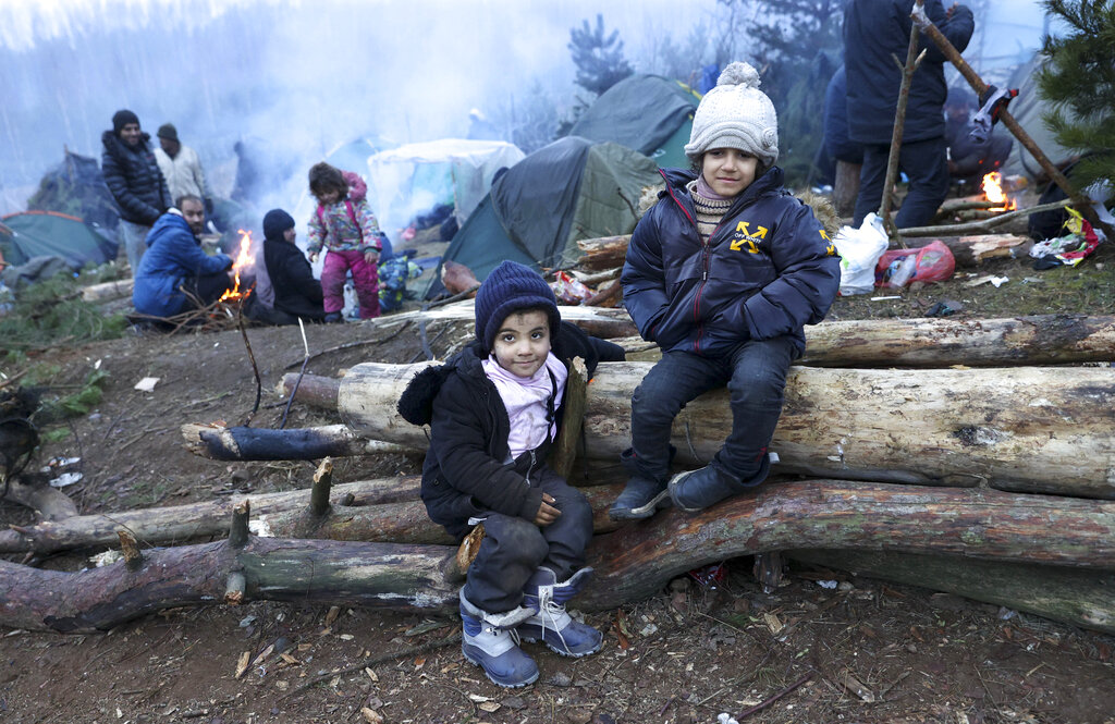 Children sit on firewood as other migrants warm themselves near fire gathering at the Belarus-Poland border near Grodno, Belarus, Sunday, Nov. 14, 2021.Poland's prime minister says Poland, Lithuania and Latvia are considering asking NATO for emergency talks as they struggle to manage a tense standoff on their borders with Belarus. The EU nations say Belarus is orchestrating a migrant crisis on their borders in retaliation for EU sanctions on Belarus for cracking down on democracy protesters. (Oksana Manchuk/BelTA pool photo via AP)