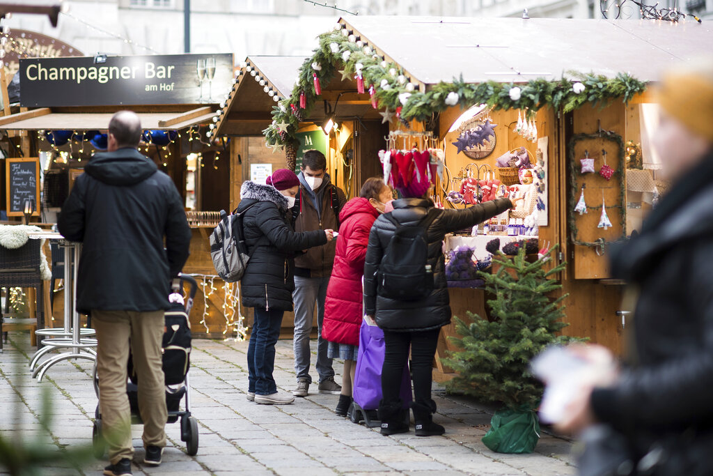People wearing face mask to protect against the coronavirus as they visits a Christmas market in Vienna, Austria, Wednesday, Nov. 17, 2021. The Austrian a nationwide lockdown for unvaccinated people is in place to combat rising coronavirus infections and deaths. (AP Photo/Michael Gruber)