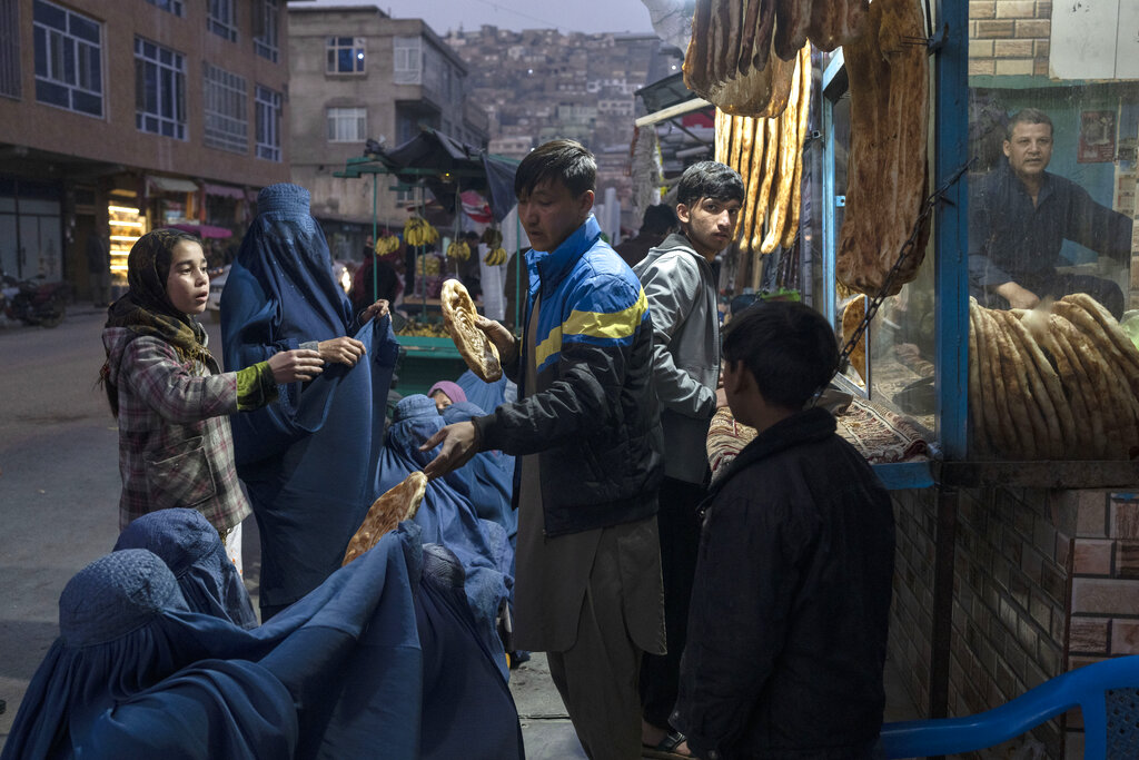 A man distributes bread to Burka-wearing Afghan women outside a bakery in Kabul, Afghanistan, Thursday, Dec, 2, 2021. According to U.N. figures from early November, almost 24 million people in Afghanistan, around 60% percent of the population, suffer from acute hunger, including 8.7 million living in near famine. Increasing numbers of malnourished children have filled hospital wards. (AP Photo/Petros Giannakouris)