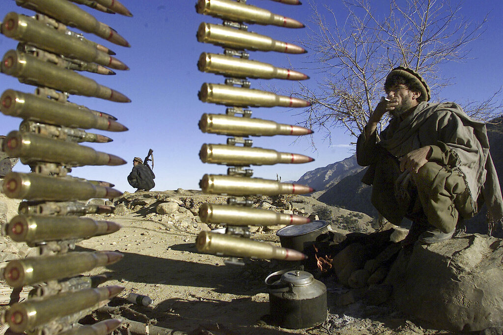 Afghan anti-al-Qaida fighters rest at a former al-Qaida base in the White Mountains near Tora Bora Wednesday Dec. 19, 2001, behind a string of ammunition found after the retreat of al-Qaida members from the area. (AP Photo/David Guttenfelder)