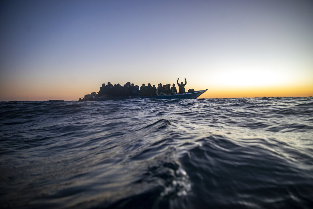 Migrants and refugees of various African nationalities wait for assistance aboard an overcrowded wooden boat in the Mediterranean Sea 122 miles off the coast of Libya as aid workers on the Spanish search and rescue vessel Open Arms approach on Feb. 12, 2021. (AP Photo/Bruno Thevenin)