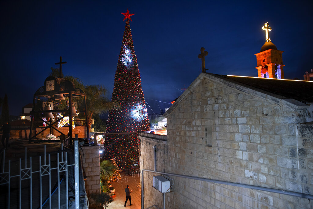 A man walks by a Christmas tree during the lighting ceremony, outside the Greek Orthodox Church of the Annunciation, in Nazareth, Israel, Sunday, Dec. 12, 2021. (AP Photo/Oded Balilty)