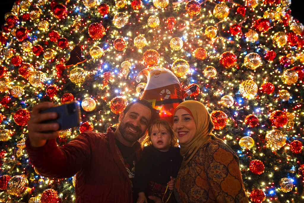 A family takes a selfie next to the Christmas tree during the lighting ceremony, outside the Greek Orthodox Church of the Annunciation, in Nazareth, Israel, Sunday, Dec. 12, 2021. (AP Photo/Oded Balilty)