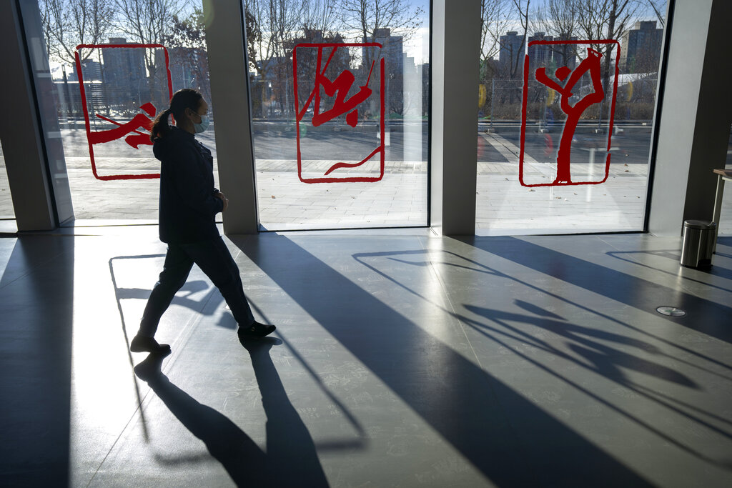 A worker walks past windows decorated with graphic renderings of winter sports at the Winter Olympic Village in Beijing, Friday, Dec. 24, 2021. Organizers on Friday gave the media a look at parts of the athletes' Olympic Village for the 2022 Winter Olympics and Paralympics, which will be held beginning in February. (AP Photo/Mark Schiefelbein)