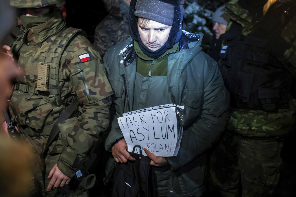 An asylum seeker from Syria who has been taken into custody by Polish border guards holds a paper saying 