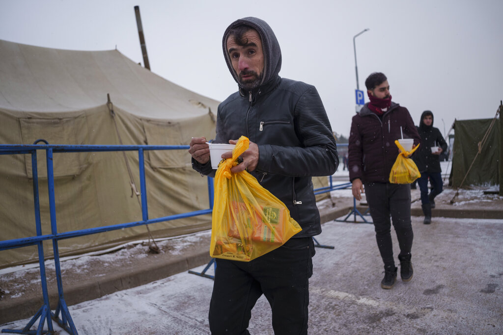 Migrants carry meal at a logistics center at the checkpoint logistics center 