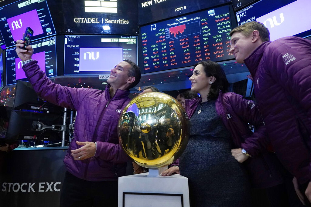 Nubank CEO David Velez, left, takes a selfie photo with his company's co-Founders Cristina Junqueira, and Edward Wible, before he rings the ceremonial first trade bell during his IPO, on the New York Stock Exchange trading floor, Thursday, Dec. 9, 2021. (AP Photo/Richard Drew)