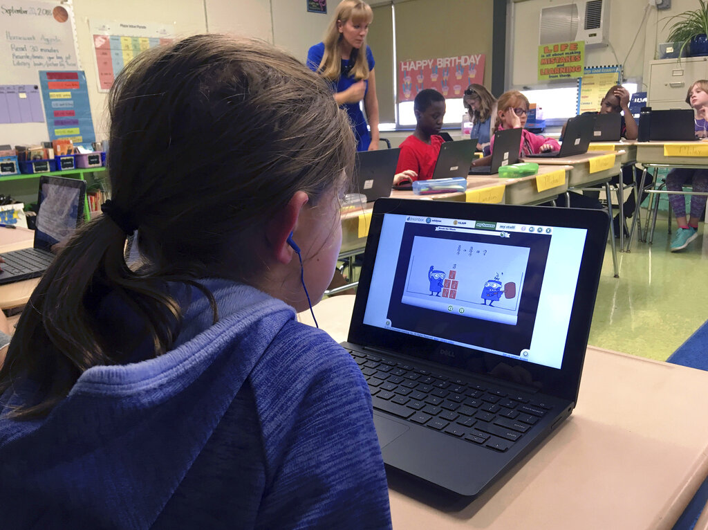 In this Sept. 20, 2018 photo, fifth grade student Ashlynn De Filippis, left, works math problems on the DreamBox system as teacher Heather Dalton, center rear, works with other students in class at Charles Barnum Elementary School in Groton, Conn. A wide array of apps, websites and software used in schools borrow elements from video games to help teachers connect with students living technology-infused lives. (AP Photo/Michael Melia)