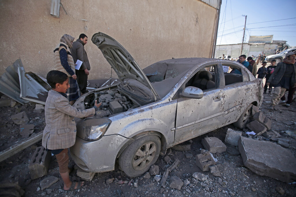 People inspect a damaged car at the site of airstrikes by a Saudi-led coalition on a workshop, in Sanaa, Yemen, Sunday, Dec. 5, 2021. The coalition fighting Iran-backed rebels in Yemen accelerated airstrikes on the capital and elsewhere in the conflict-stricken country in recent weeks, as government forces advanced in the west coast and the key province of Marib, officials said Sunday. (AP Photo/Hani Mohammed)