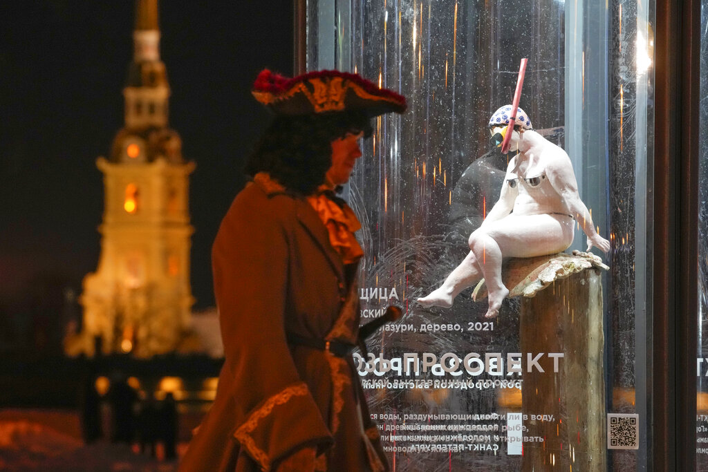 A street actor wearing a period costume walks past a sculpture 'Woman-Diver' by sculptor Ivan Asinovsky at a street exhibition in St. Petersburg, Russia, Friday, Jan. 7, 2022. (AP Photo/Dmitri Lovetsky)