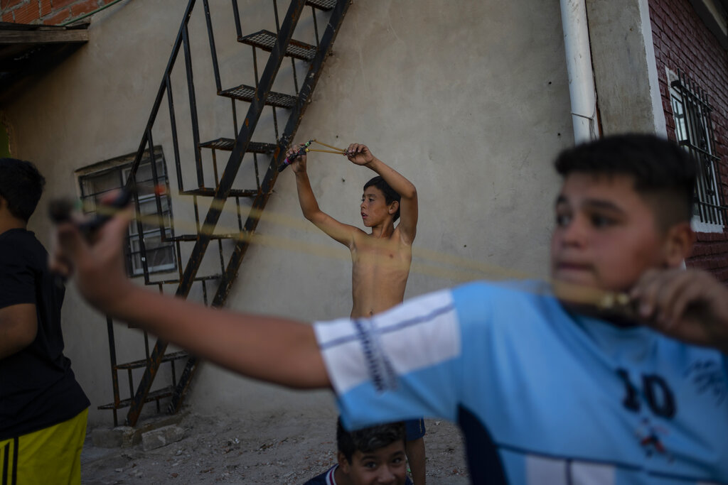 Boys shoot birds with their slingshots at Puerta 8, a low income neighborhood north of Buenos Aires, Argentina, Wednesday, Feb. 10, 2022, where contaminated cocaine may have been sold. A batch of that toxic cocaine has killed at least 23 people and hospitalized many more, according to police. (AP Photo/Rodrigo Abd)
