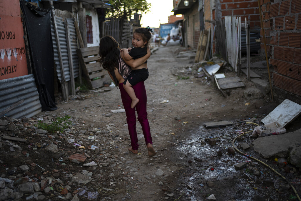 A girl carries a toddler in Puerta 8, a low income neighborhood north of Buenos Aires, Argentina, Wednesday, Feb. 9, 2022, where contaminated cocaine may have been sold. A batch of that toxic cocaine has killed at least 23 people and hospitalized many more, according to police. (AP Photo/Rodrigo Abd)