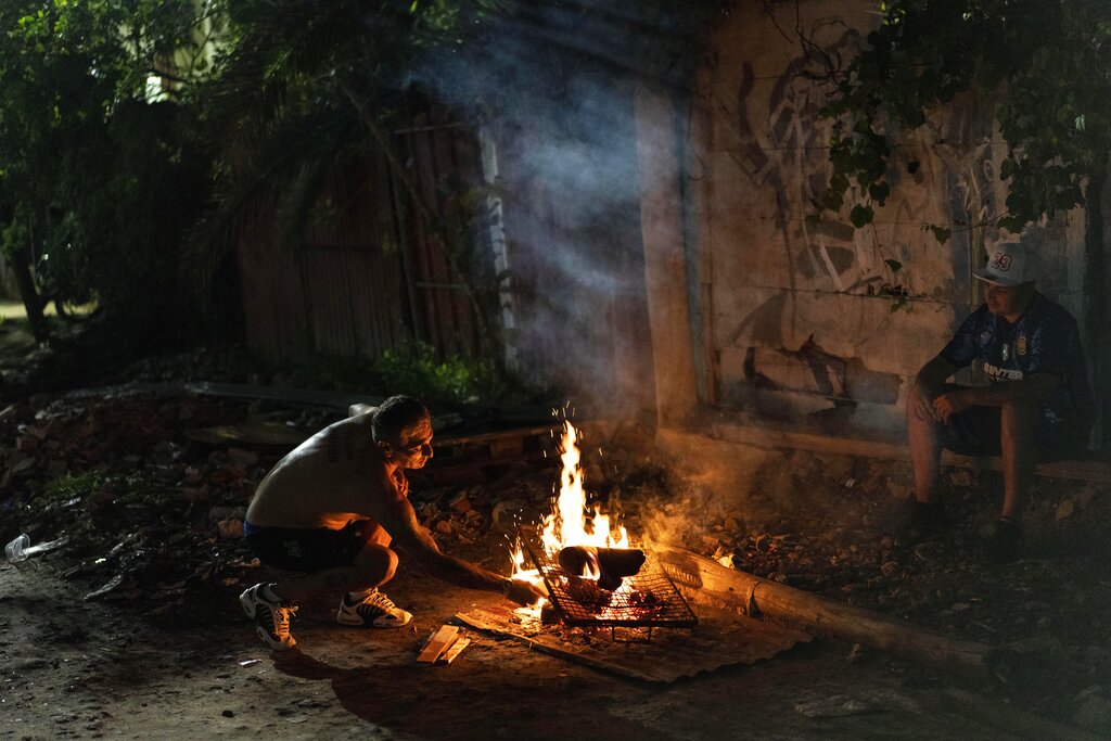 A man builds a fire to prepare a meal at the entrance of the Puerta 8 neighborhood, a suburb north of Buenos Aires, Argentina, Friday, Feb. 4, 2022, where police say contaminated cocaine may have been sold. A batch of toxic cocaine has killed at least 23 people and hospitalized many more in Argentina, according to police. (AP Photo/Rodrigo Abd)