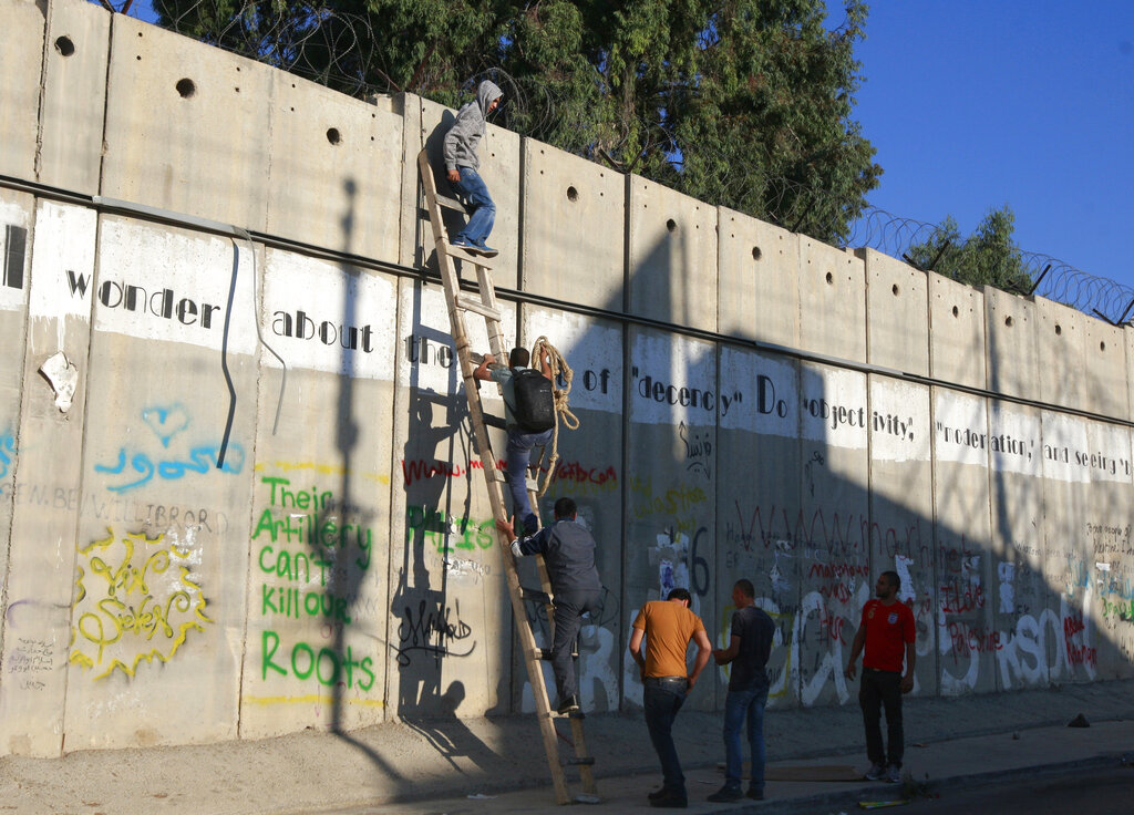 FILE - In this Friday, Aug. 2, 2013, file photo,  Palestinians use a ladder to climb over the separation barrier with Israel on their way to pray at the al-Aqsa Mosque in Jerusalem during the Muslim holy month of Ramadan, in Al-Ram, north of Jerusalem. John Kerrys warning that Israel could become an apartheid state if it doesnt reach a peace deal with the Palestinians has set off an uproar in Israel and angered Israels allies in Washington. Kerry was forced to backtrack from his comments, but he voiced an opinion that is frequently heard in Israel itself and tapped into a debate that has become increasingly heated in recent years. (AP Photo/Majdi Mohammed, File)