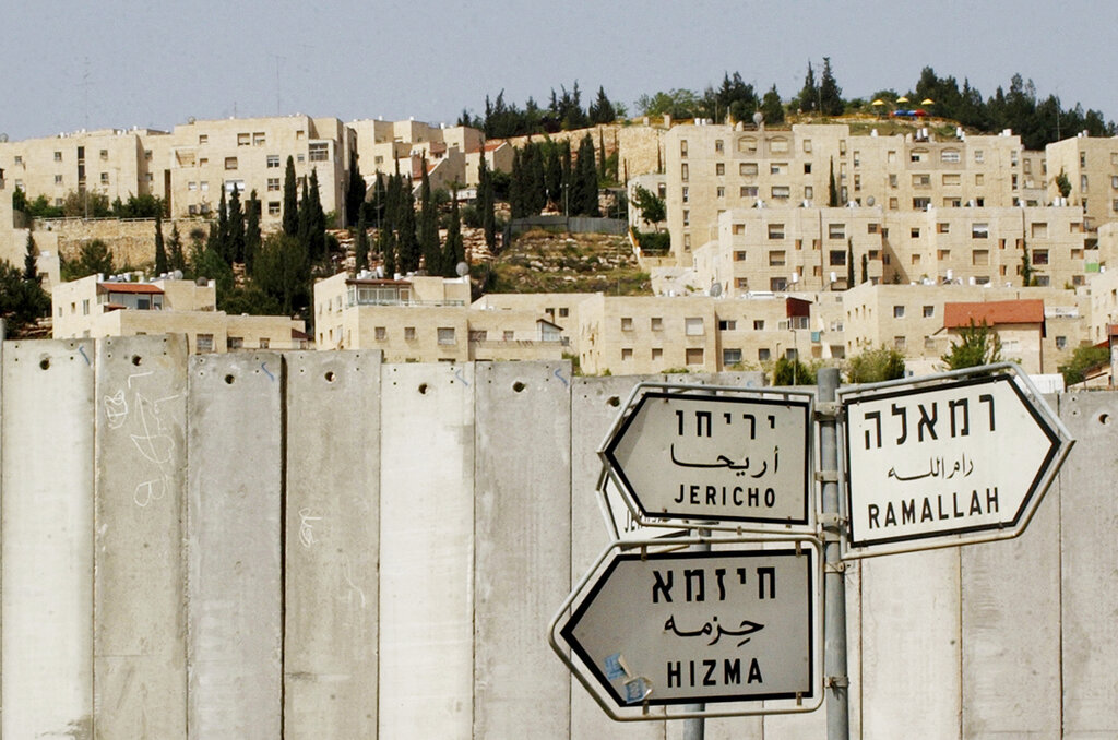 FILE - The Jewish settlement of Pisgat Ze'ev is visible behind a section of Israel's separation barrier, as road signs point to the Palestinian towns of Jericho, Ramallah, and Hizma, in the west Bank village of Hizma, near Jerusalem, April 14, 2005. Israel on Monday, Jan. 31, 2022, called on Amnesty International not to publish an upcoming report accusing it of apartheid, saying the conclusions of the London-based international human rights group are “false, biased and antisemitic.” (AP Photo/Muhammed Muheisen, File)