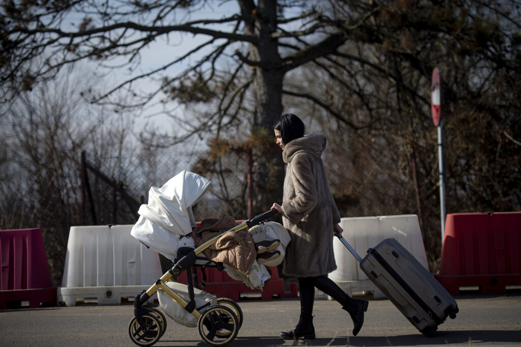 A woman pushes a baby stroller after crossing the border from Ukraine at the Romanian-Ukrainian border, in Siret, Romania, Friday, Feb. 25, 2022. Thousands of Ukrainians are fleeing from war by crossing their borders to the west in search of safety. They left their country as Russia pounded their capital and other cities with airstrikes for a second day on Friday. Cars were backed up for several kilometers (miles) at some border crossings as authorities in Poland, Slovakia, Hungary, Romania and Moldova mobilized to receive them, offering them shelter, food and legal help. (AP Photo/Alexandru Dobre)