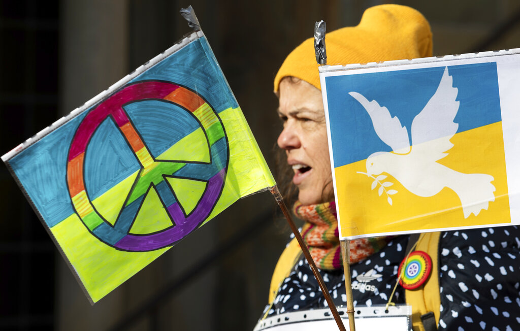 A woman holds flags with the peace symbol and a peace dove in the national colors of Ukraine in Osnabrueck, Germany, Saturday, Feb. 26, 2022. A prayer for peace in St. Mary's Church later leads to a silent march against Russia's attack on Ukraine. (Friso Gentsch/dpa via AP)