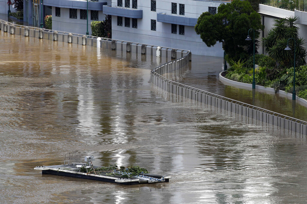 An unhinged pontoon drifts past apartments on the river in Brisbane, Australia, Wednesday, March 2, 2022. Tens of thousands of people had been ordered to evacuate their homes and many more had been told to prepare to flee as parts of Australia's southeast coast are inundated by the worst flooding in decades. (AP Photo/Tertius Pickard)