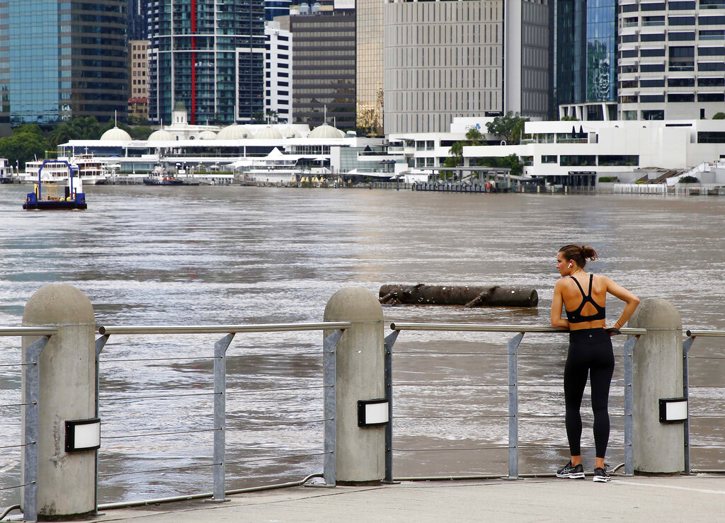 A jogger pauses to watch debris float down the Brisbane river in Brisbane, Australia, Wednesday, March 2, 2022. Tens of thousands of people had been ordered to evacuate their homes and many more had been told to prepare to flee as parts of Australia's southeast coast are inundated by the worst flooding in decades. (AP Photo/Tertius Pickard)