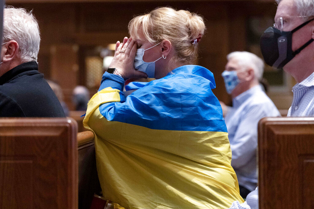 Parishioner 0lena Ftomova draped in a Ukrainian flag, prays during the Ash Wednesday mass which  marks the beginning of Lent at Saint Matthew the Apostle Cathedral in Washington, Wednesday, March, 2, 2022. ( AP Photo/Jose Luis Magana)