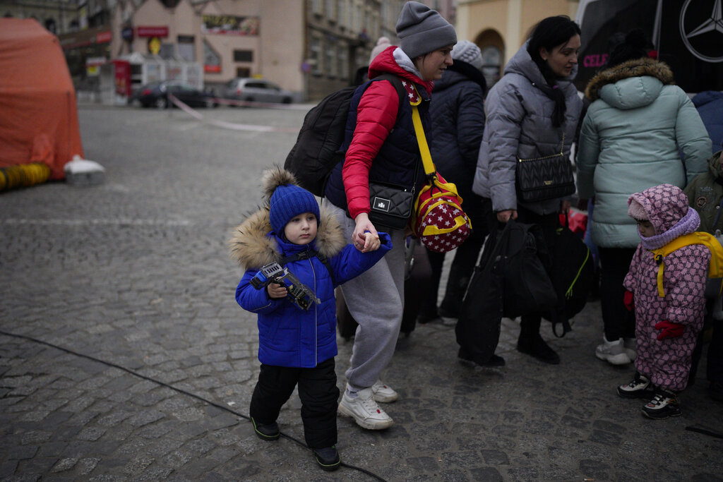A woman holds the hand of a child, as they travel with others who have fled Ukraine, at the at the train station in Przemysl, Poland, Tuesday, March 8, 2022. U.N. officials said Tuesday that the Russian onslaught has forced 2 million people to flee Ukraine. (AP Photo/Daniel Cole)