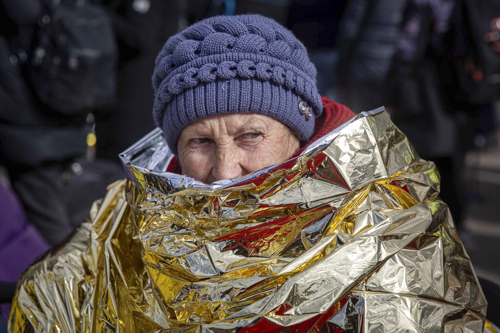 A woman wrapped in thermal blanket fleeing from Ukraine, waits to board a bus at the border crossing in Medyka, Poland, Poland, Tuesday, March 8, 2022. Russia's invasion of Ukraine has set off the largest mass migration in Europe in decades, with more than 1.5 million people having crossed from Ukraine into neighboring countries. (AP Photo/Visar Kryeziu)