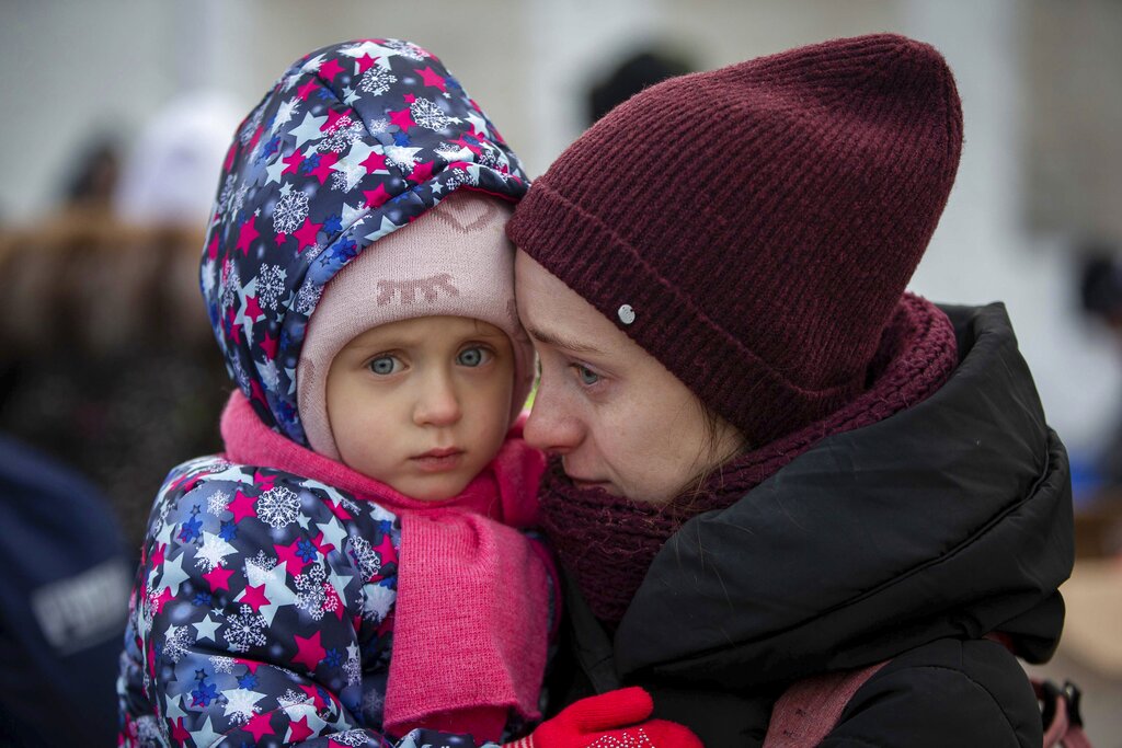 A mother and her child, fleeing Ukraine, wait to board a bus at the border crossing in Medyka, Poland, Poland, Tuesday, March 8, 2022. Russia's invasion of Ukraine has set off the largest mass migration in Europe in decades, with more than 1.5 million people having crossed from Ukraine into neighboring countries. (AP Photo/Visar Kryeziu)