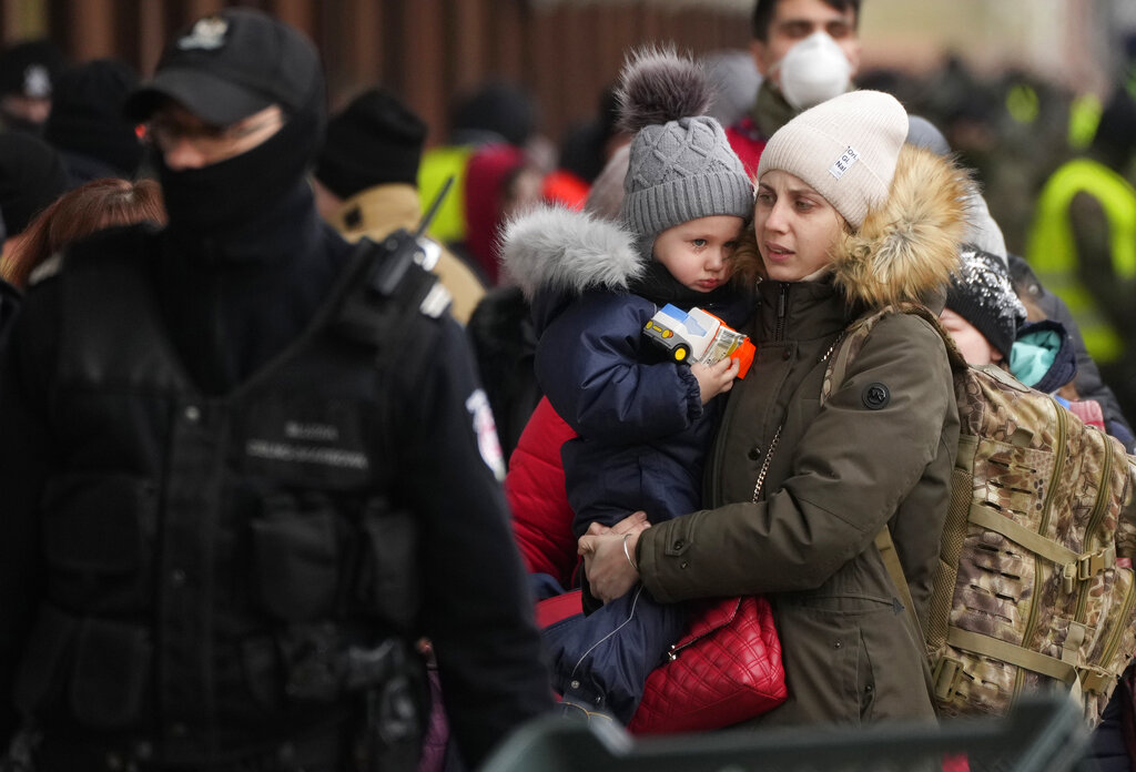 A woman holds a child as she walks with others, after disembarking from a train originating in Lviv, Ukraine, at the station in Przemysl, Poland, Monday, March 7, 2022. Russia's invasion of Ukraine has set off the largest mass migration in Europe in decades, with more than 1.5 million people having crossed from Ukraine into neighboring countries. (AP Photo/Czarek Sokolowski)