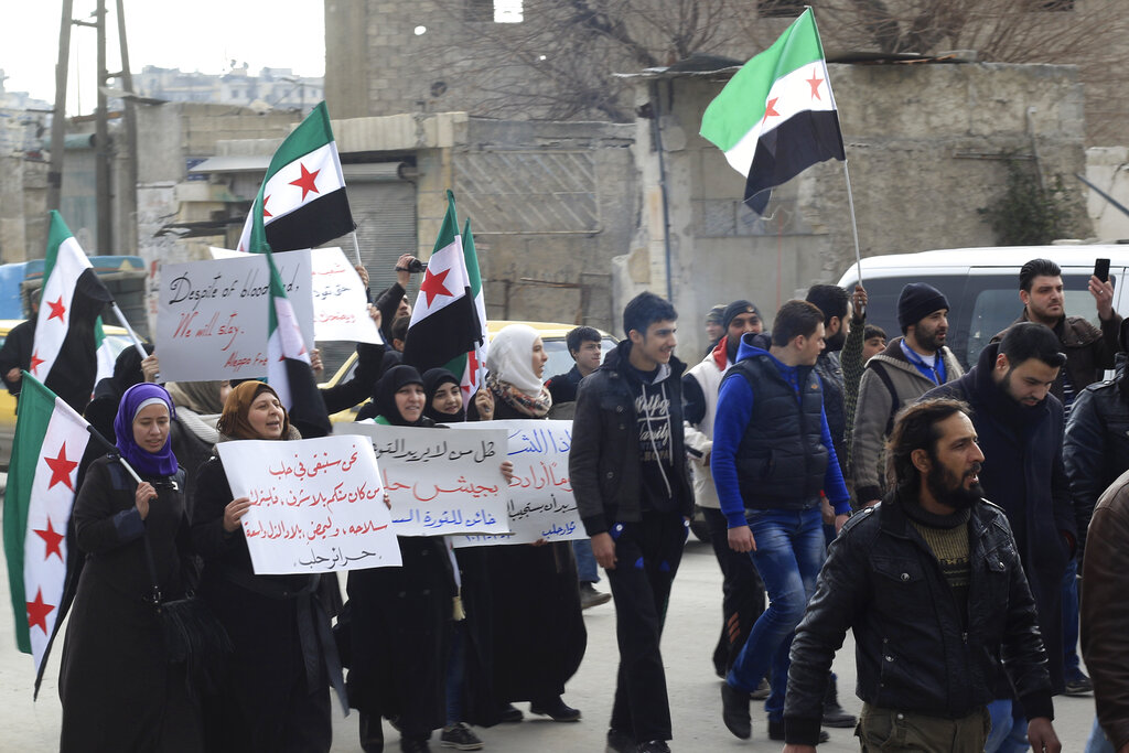 This photo provided by Afraa Hashem in March 2022, shows her, second left, with other protesters holding anti-Bashar Assad signs during a rally east of Aleppo, Syria. Hashem and other Aleppo survivors on Tuesday, March 15, 2022, mark the 11th anniversary of Syria's revolution-turned-civil war. This year, many survivors are watching in shock as Ukrainians face the same horrors they did. (Milad al-Shehabi via AP)