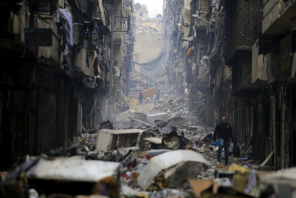 FILE - Residents walk through the destruction of the once rebel-held Salaheddine neighborhood in the eastern Aleppo, Syria, Friday, Jan. 20, 2017. Tuesday, March 15, 2022 marks the 11th anniversary of Syria's revolution-turned-civil war. This year, many survivors are watching in shock as Ukrainians face the same horrors they did. (AP Photo/Hassan Ammar, File)