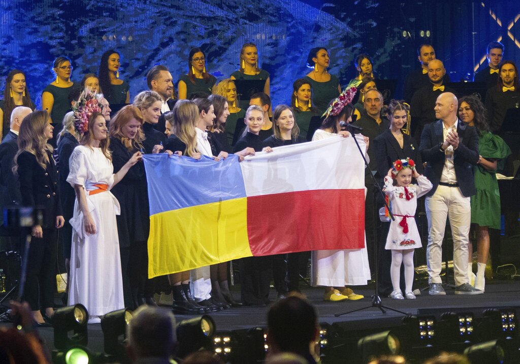 Seven-year-old Amellia Anisovych, a refugee from Ukraine, holds her headdress as she stands next to a polish flag in the finale of a fund-raising concert in Lodz, Poland, Sunday, March 20, 2022. Anisovych opened the concert by singing Ukraine's national anthem. She became widely known for singing of a song from the movie Frozen in a bomb shelter in Kyiv in early March. She has since come to Poland with her grandmother and brother. Her parents remained in Kyiv. (AP Photo/Marian Zubrzycki)