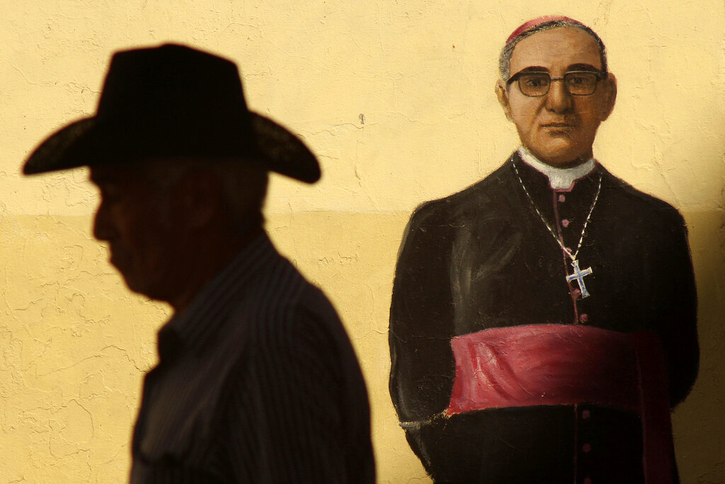 FILE - In this  Saturday, March 24, 2018 filer, a man walks past a mural depicting the late Archbishop Oscar Arnulfo Romero on an exterior wall of the Metropolitan Cathedral where a Mass was offered to mark the anniversary of the archbishop's death, in San Salvador, El Salvador. Pope Francis has moved the Rev. Rutilio Grande, a Jesuit priest who inspired St. Oscar Romero and was himself a victim of El Salvador's right-wing death squads, a step closer to possible sainthood. Francis approved a decree Friday, Feb. 21, 2020 proclaiming Grande a martyr for the Catholic faith. (AP Photo/Salvador Melendez, File)