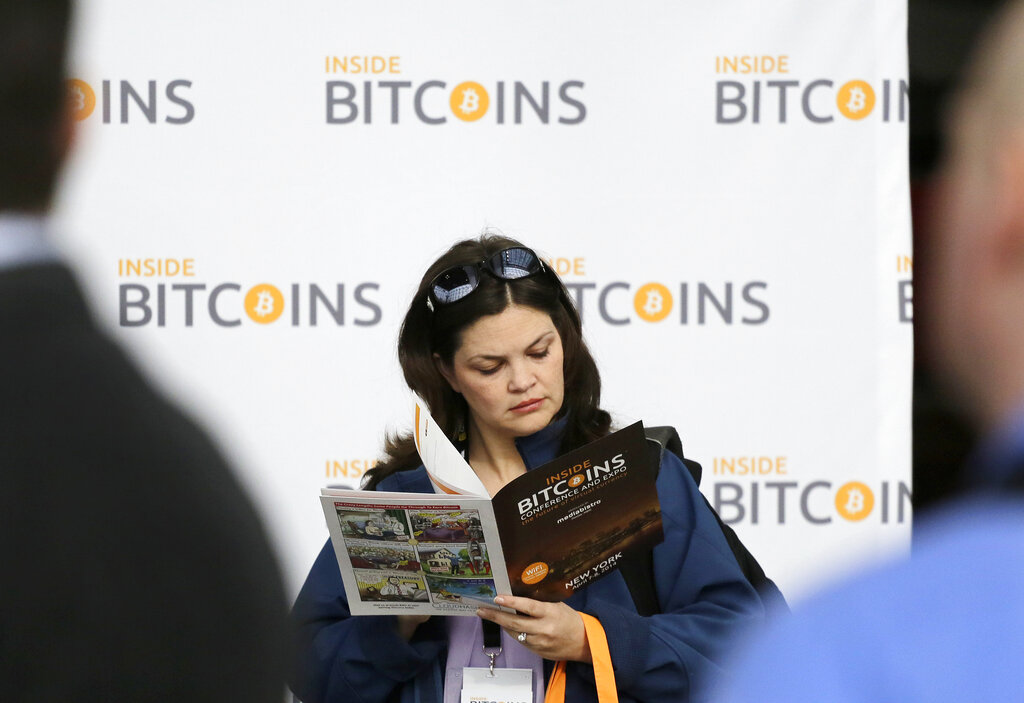 A woman reads about bitcoin while attending the Inside Bitcoins conference and trade show, Monday, April 7, 2014 in New York. Bitcoin users exchange cash for digital money using online exchanges, then store it in a computer program that serves as a wallet. The program can transfer payments directly to merchants or individuals around the world, eliminating transaction fees and the need for bank or credit card information. (AP Photo/Mark Lennihan)