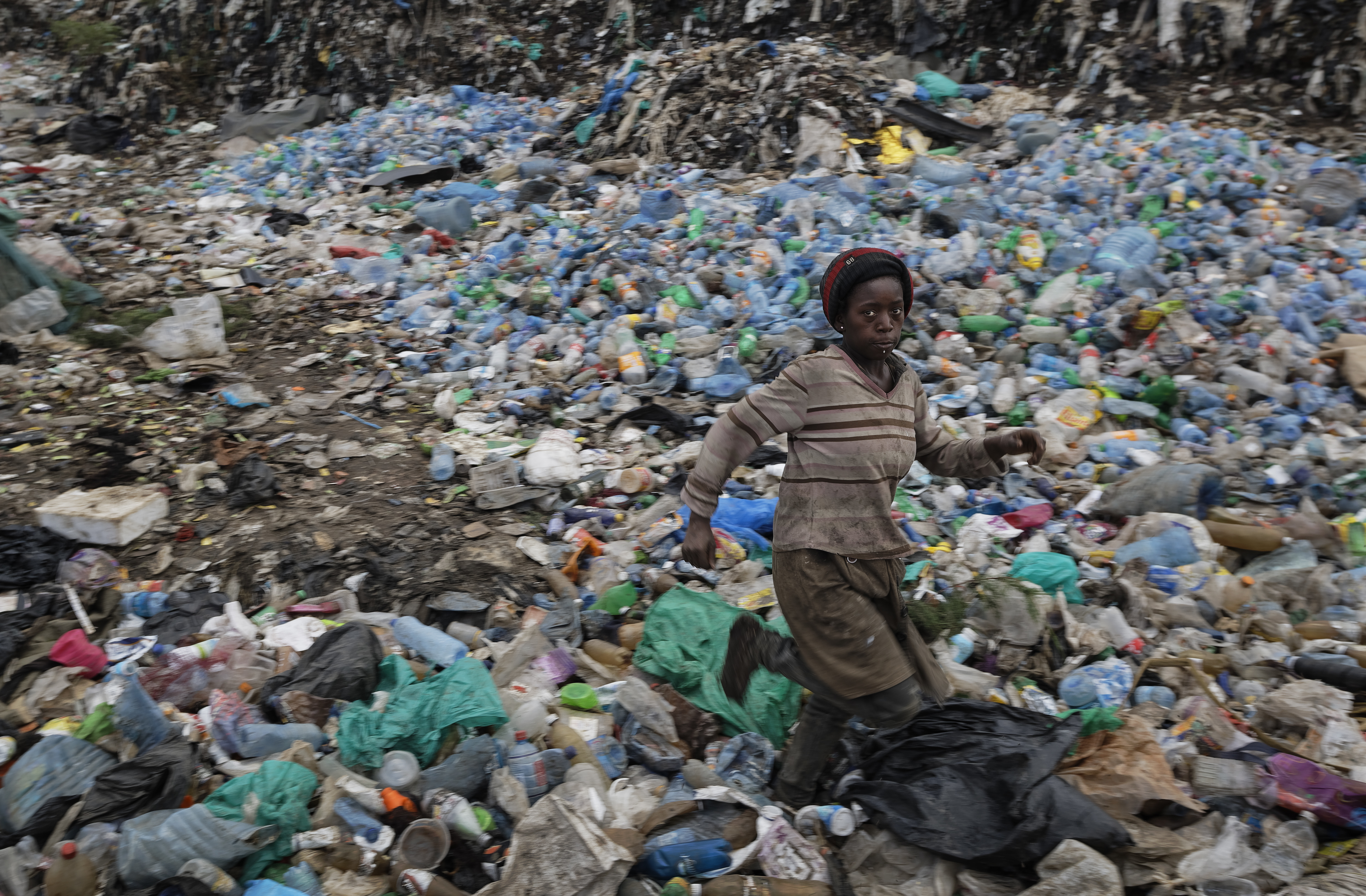 In this photo taken Wednesday, Dec. 5, 2018, a young girl who scavenges for recyclable materials for a living runs through a mound of sorted plastic bottles at the dump in the Dandora slum of Nairobi, Kenya. As the world meets again to tackle the growing threat of climate change, how the continent tackles the growing solid waste produced by its more than 1.2 billion residents, many of them eager consumers in growing economies, is a major question in the fight against climate change. (AP Photo/Ben Curtis)