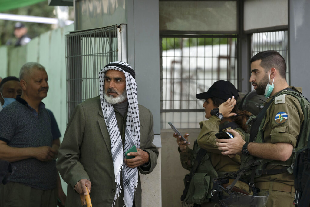 Israeli soldiers speak with a Palestinian man crossing from the West Bank town of Bethlehem into Jerusalem for the first Friday prayers in the Muslim holy month of Ramadan at the Al Aqsa mosque compound in Jerusalem's Old City, Friday, April 8, 2022. (AP Photo/Maya Alleruzzo)