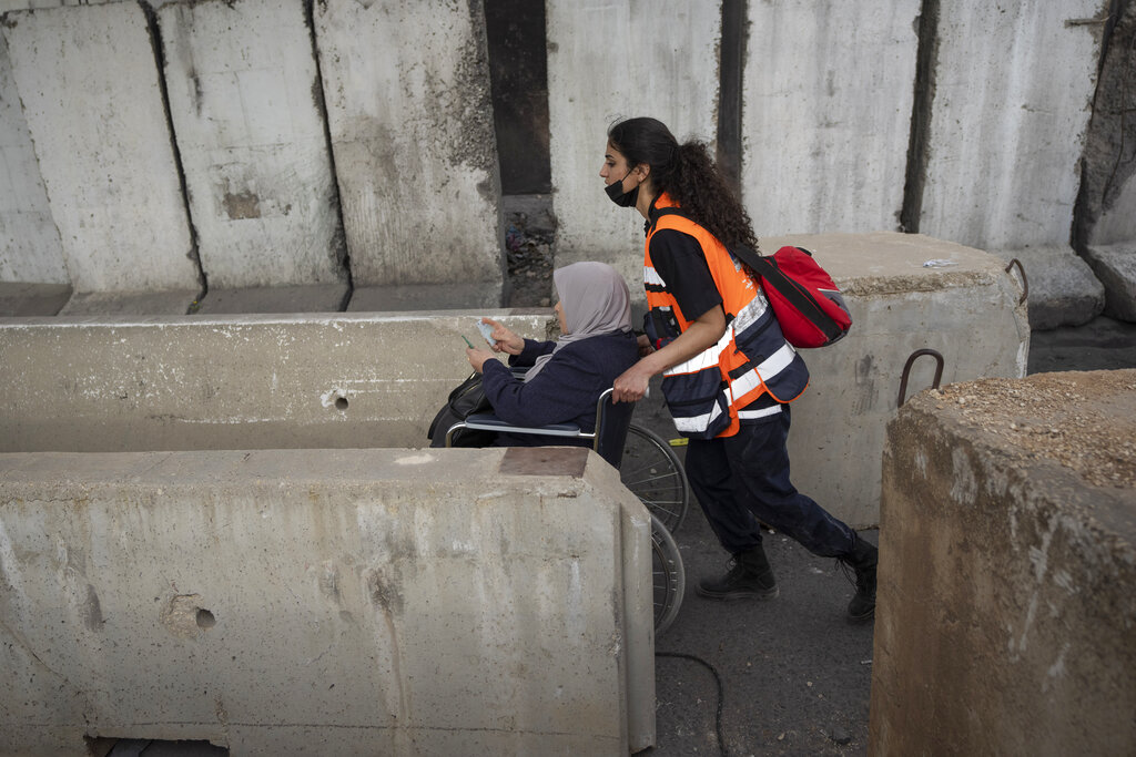 A paramedic helps a Palestinian woman on a wheelchair to cross from the West Bank into Jerusalem, for the first Friday prayers in the Muslim holy month of Ramadan at the Al Aqsa mosque compound, through the Qalandia Israeli army checkpoint, west of Ramallah, Friday, April 8, 2022. (AP Photo/Nasser Nasser)