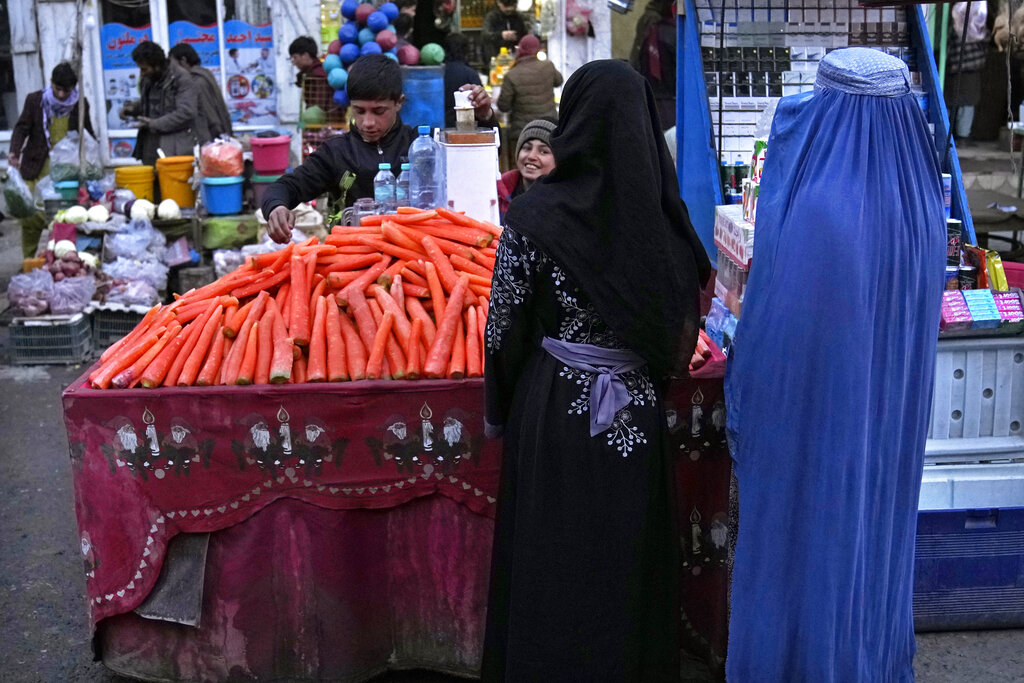 An Afghan woman, right, drinks carrots juice under her burqa, at an outdoor market, in Kabul, Afghanistan, Sunday, Feb. 20, 2022. (AP Photo/Hussein Malla)