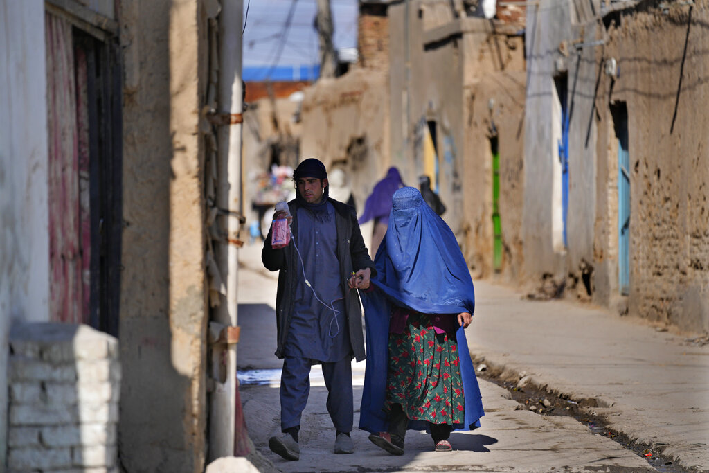 A man holds an IV bag for his sick wife as they enter their house, in Kabul, Afghanistan, Sunday, Feb. 20, 2022. (AP Photo/Hussein Malla)